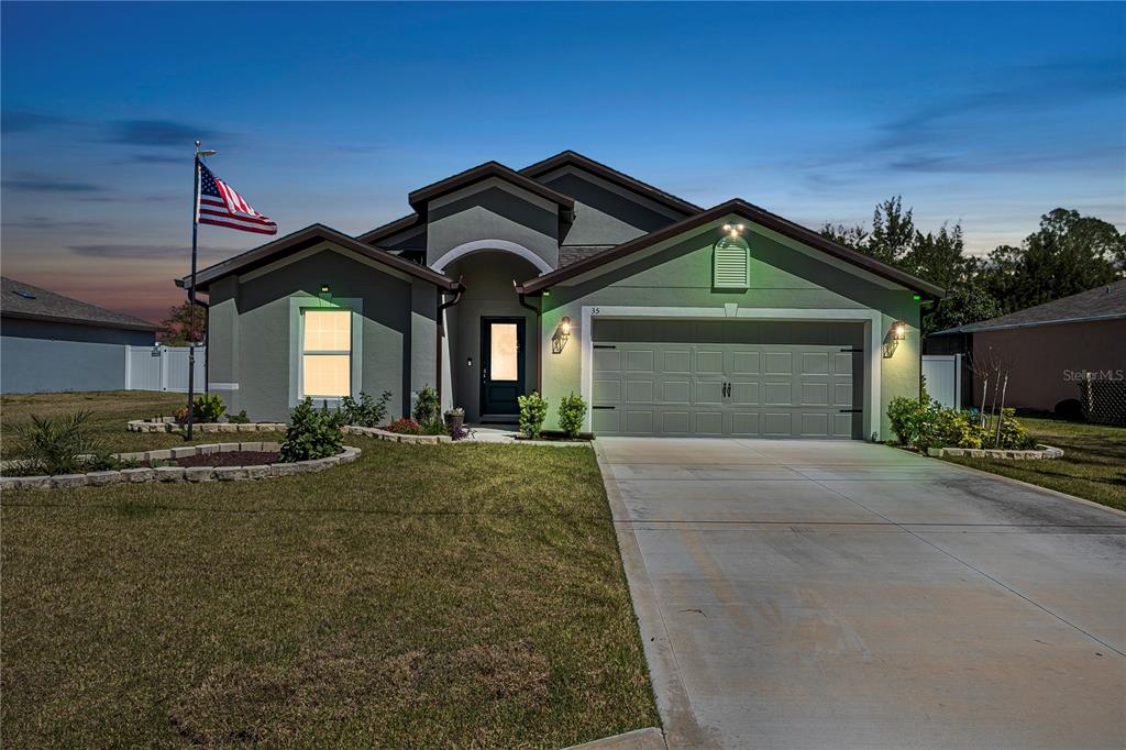 A single-story house with a gray stucco exterior, a two-car garage, and an American flag — 35 ROLLINS LANE, PALM COAST, FL