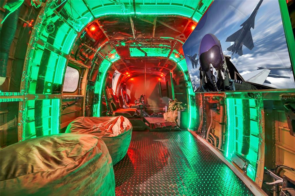 A room inside a converted aircraft fuselage features green LED lighting, beanbag chairs, and a television — 1213 RADIANT STREET, REUNION, FL