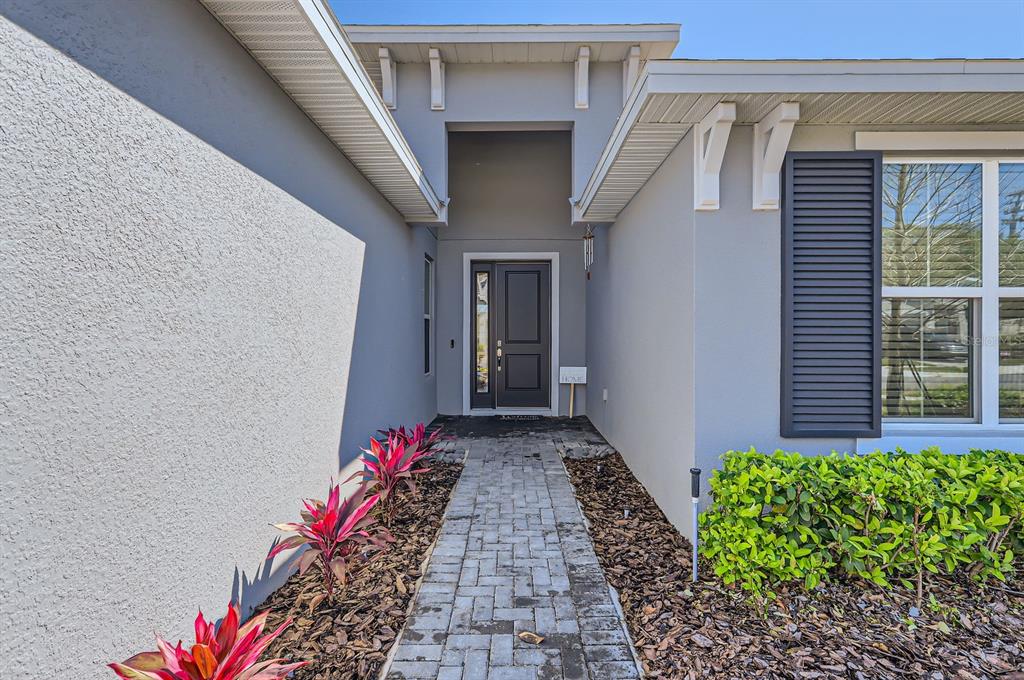 A paved walkway leads to the front entrance of a house with gray stucco siding — 2372 SIRENA LANE, MOUNT DORA, FL