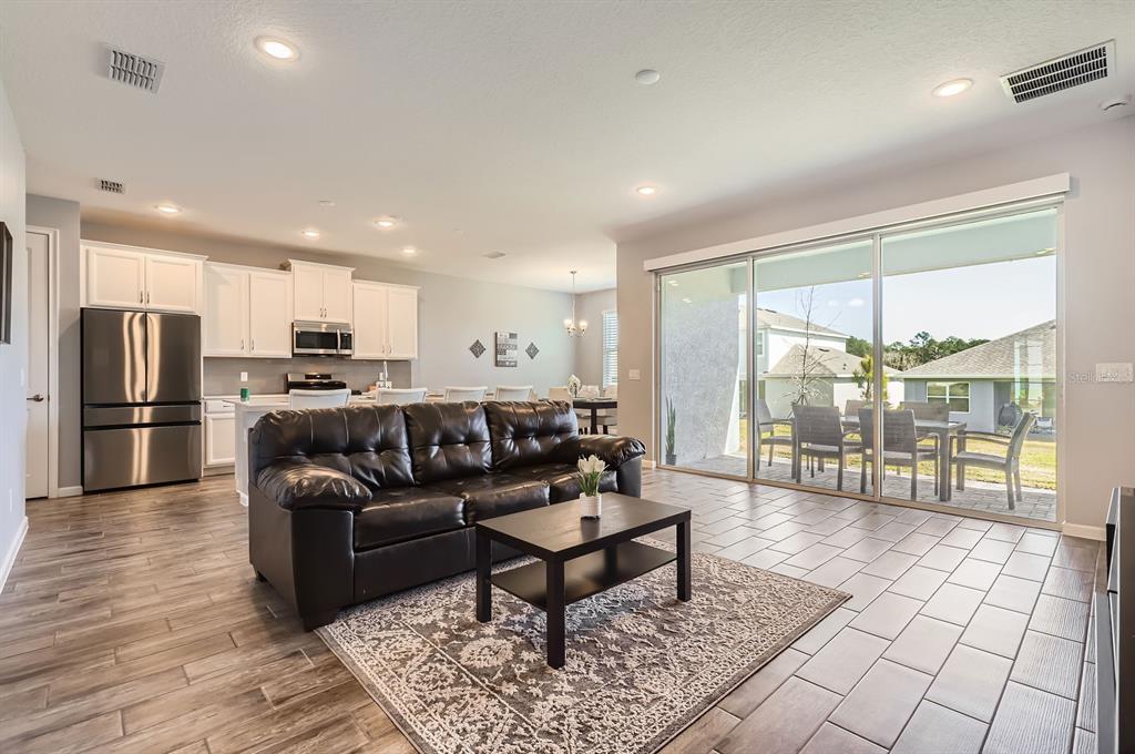 An open-concept living room with tile flooring, a black leather sofa, and sliding glass doors — 2372 SIRENA LANE, MOUNT DORA, FL