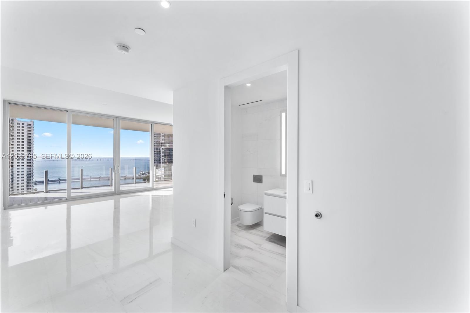 A bright room with white marble floors leads to a bathroom and a balcony view — 300 Biscayne Blvd Way # 1802, Miami FL 33131, MIAMI, FL