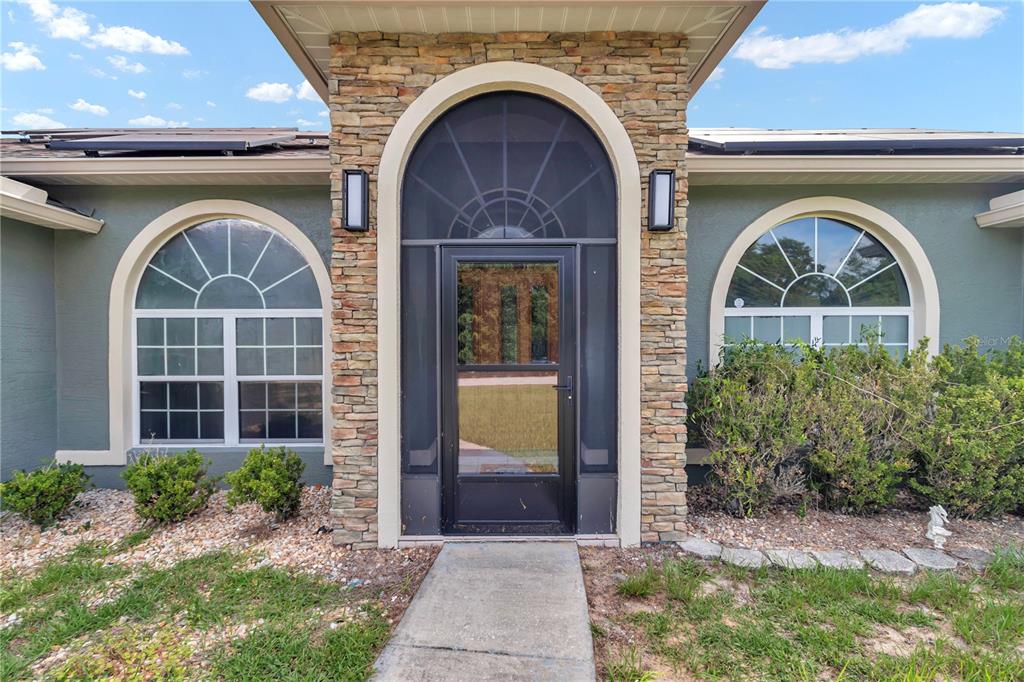 The front exterior of a house features a stone-accented entryway with an arched screen door — 14147 SW 33 CT ROAD, OCALA, FL