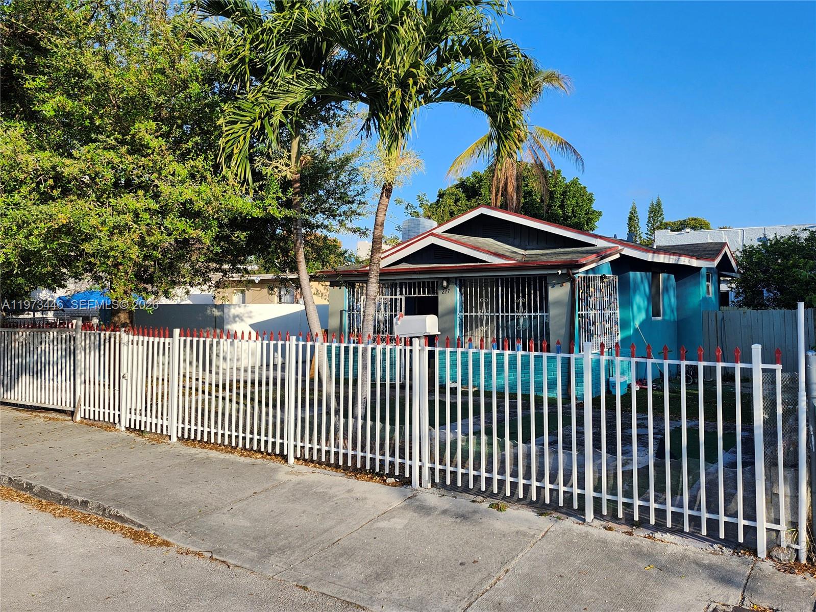 A blue house with a white metal fence and palm trees stands along a sidewalk — 227 NW 33rd St, Miami FL 33127, MIAMI, FL