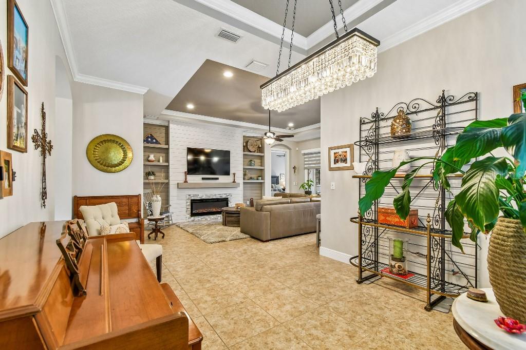 A living room features a fireplace, built-in shelving, tile flooring, and a large crystal chandelier — 112 SUFFOLK COURT, DELAND, FL