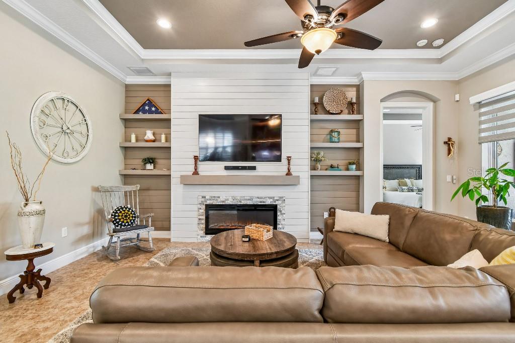 A living room features a shiplap fireplace, built-in shelves, a leather sectional, and a ceiling fan — 112 SUFFOLK COURT, DELAND, FL