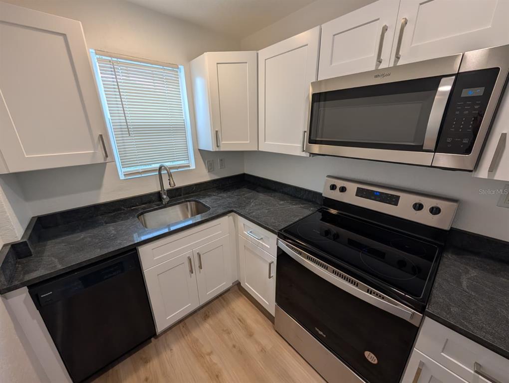 A kitchen features white cabinets, dark countertops, stainless steel appliances, and light wood-look flooring — 1834 28TH AVENUE N, ST PETERSBURG, FL