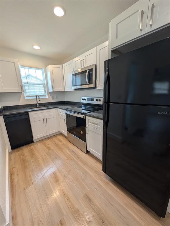A kitchen features white cabinets, stainless steel appliances, a black refrigerator, and light wood flooring — 1834 28TH AVENUE N, ST PETERSBURG, FL