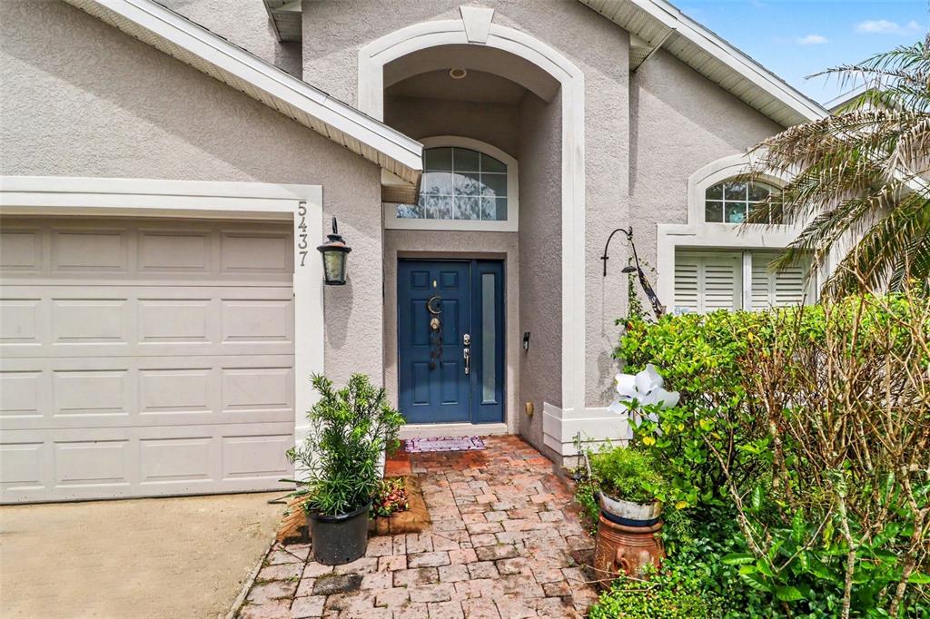The exterior of a house features a blue front door, brick walkway, and garage — 5437 FLORENCE HARBOR DRIVE, ORLANDO, FL