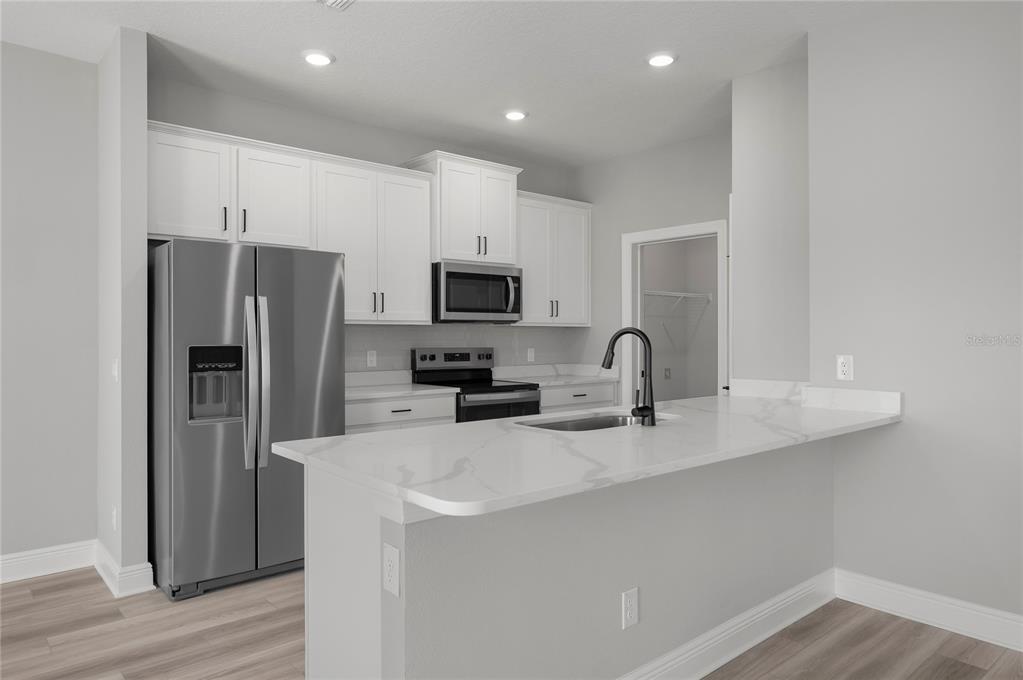 A kitchen features white cabinets, stainless steel appliances, and a white marble-look countertop island — 3348 CHINOTTO DRIVE, LAKE ALFRED, FL