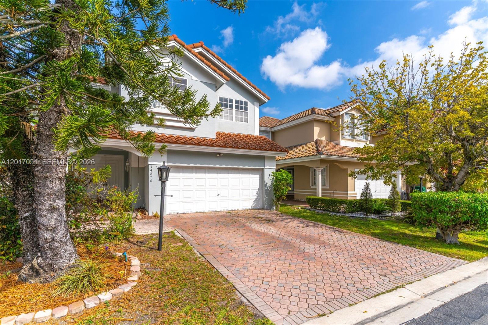 A two-story house with a brick driveway and a tile roof stands under a blue sky — 14876 SW 132nd Ave, Miami FL 33186, MIAMI, FL