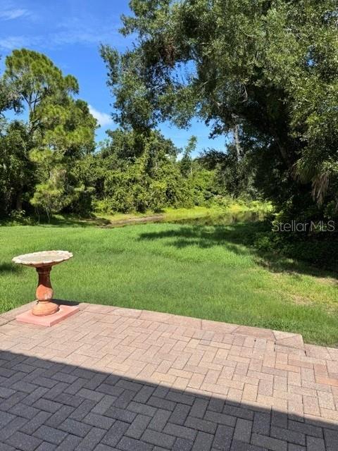 A stone patio overlooks a grassy backyard with a birdbath and a wooded area — 4727 CARRINGTON CIRCLE, SARASOTA, FL