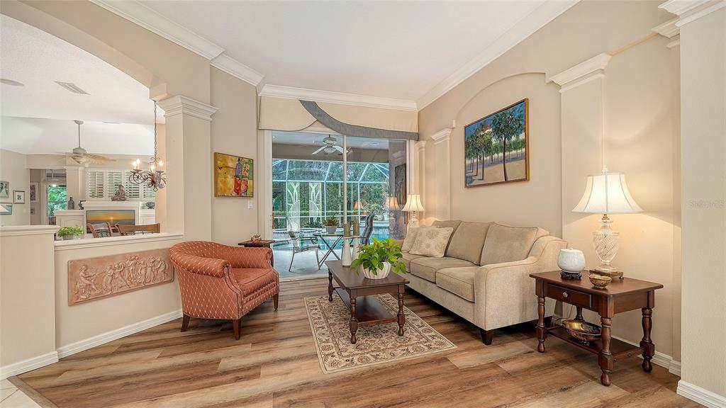 A living room with wood-look flooring, a beige sofa, an armchair, and a sliding glass door — 4727 CARRINGTON CIRCLE, SARASOTA, FL