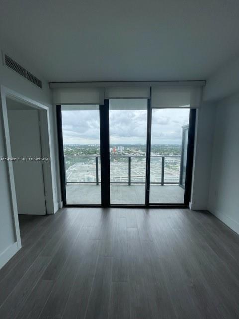 An empty room with wood-look flooring and floor-to-ceiling windows leading to a balcony — 121 NE 34th St # 2110, Miami FL 33137, MIAMI, FL