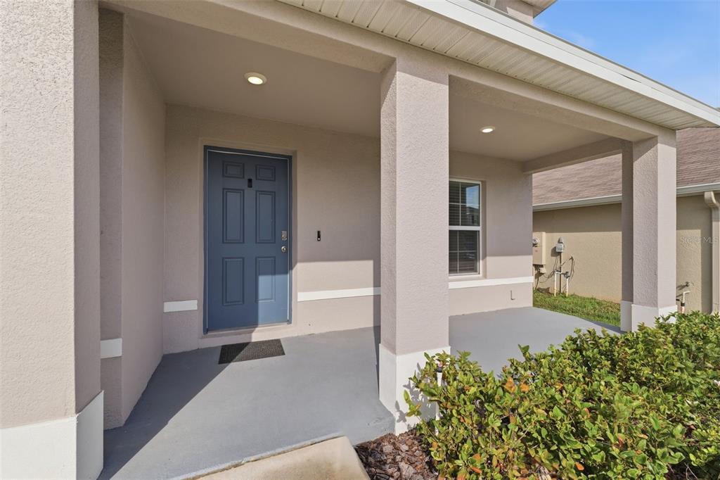A covered concrete front porch features a blue door and beige stucco exterior walls — 7517 GARDNER STREET, BROOKSVILLE, FL
