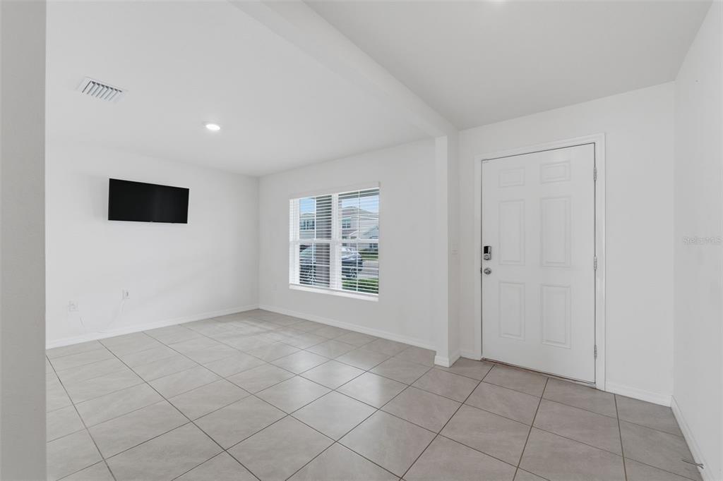 A bright, empty room features white walls, light gray tile flooring, a window, and a door — 7517 GARDNER STREET, BROOKSVILLE, FL