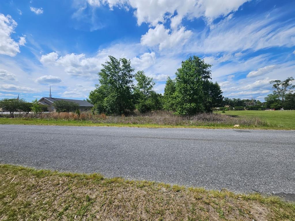 A paved road runs in front of a vacant, grassy lot with trees and a church — SE 140TH STREET, SUMMERFIELD, FL