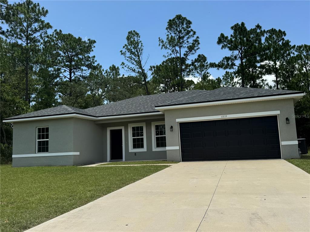 A single-story house with a gray stucco exterior, a dark garage door, and a concrete driveway — 6839 SW 149TH LANE ROAD, OCALA, FL