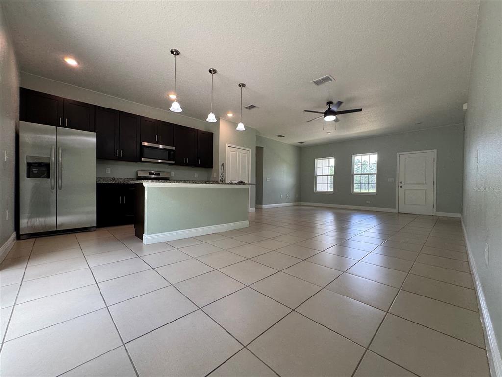 An open-concept kitchen with dark cabinets and a breakfast bar overlooks a tiled living area — 6839 SW 149TH LANE ROAD, OCALA, FL