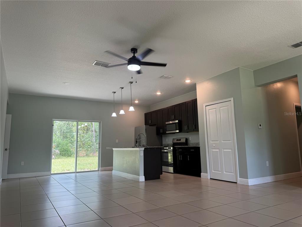 An open-concept kitchen with dark cabinets and an island overlooks a tiled living area — 6839 SW 149TH LANE ROAD, OCALA, FL