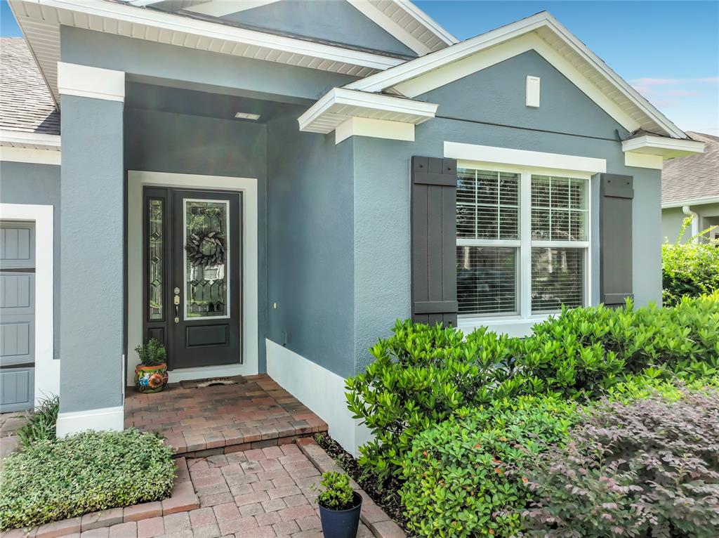 A gray front door with a decorative wreath sits next to a garage on a brick walkway — 31920 GEOFF WAY, SORRENTO, FL