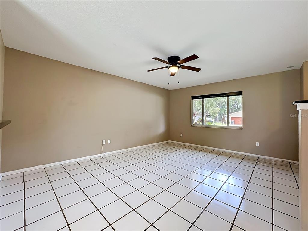 An empty room features beige walls, white tiled flooring, and a ceiling fan — 601 BRENTWOOD PLACE, BRANDON, FL
