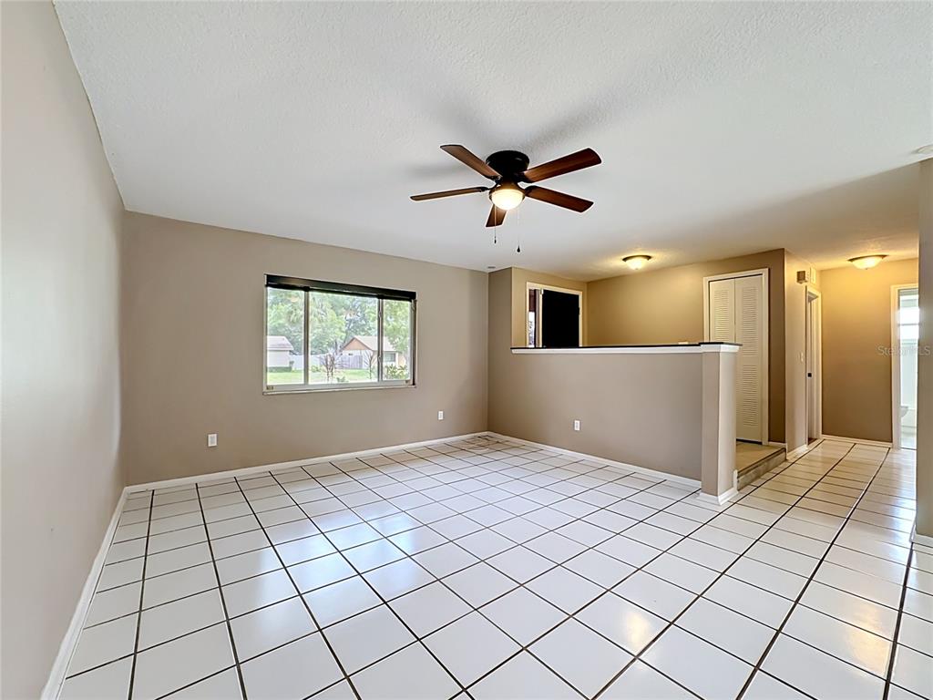 An empty room features white tiled floors, beige walls, a ceiling fan, and a half wall — 601 BRENTWOOD PLACE, BRANDON, FL