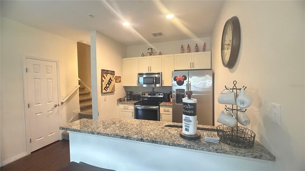 A kitchen features granite countertops, white cabinets, stainless steel appliances, and a breakfast bar — 2903 EDENSHIRE WAY UNIT 102, KISSIMMEE, FL