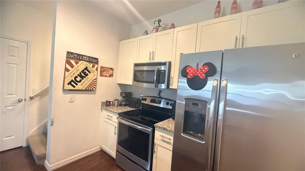 A kitchen features white cabinets, stainless steel appliances, granite countertops, and Disney-themed decor — 2903 EDENSHIRE WAY UNIT 102, KISSIMMEE, FL