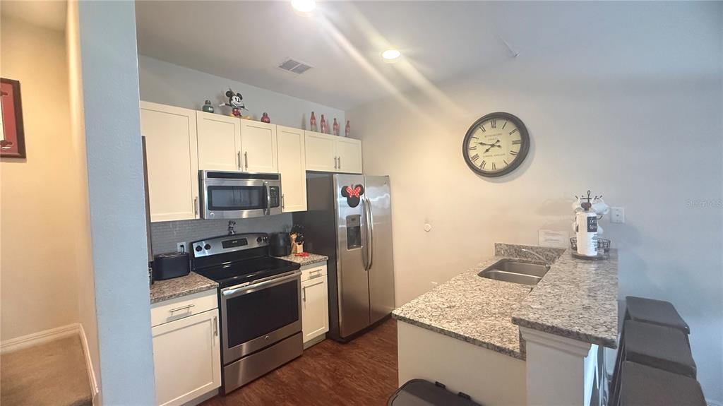 A kitchen features white cabinets, stainless steel appliances, granite countertops, and a breakfast bar — 2903 EDENSHIRE WAY UNIT 102, KISSIMMEE, FL