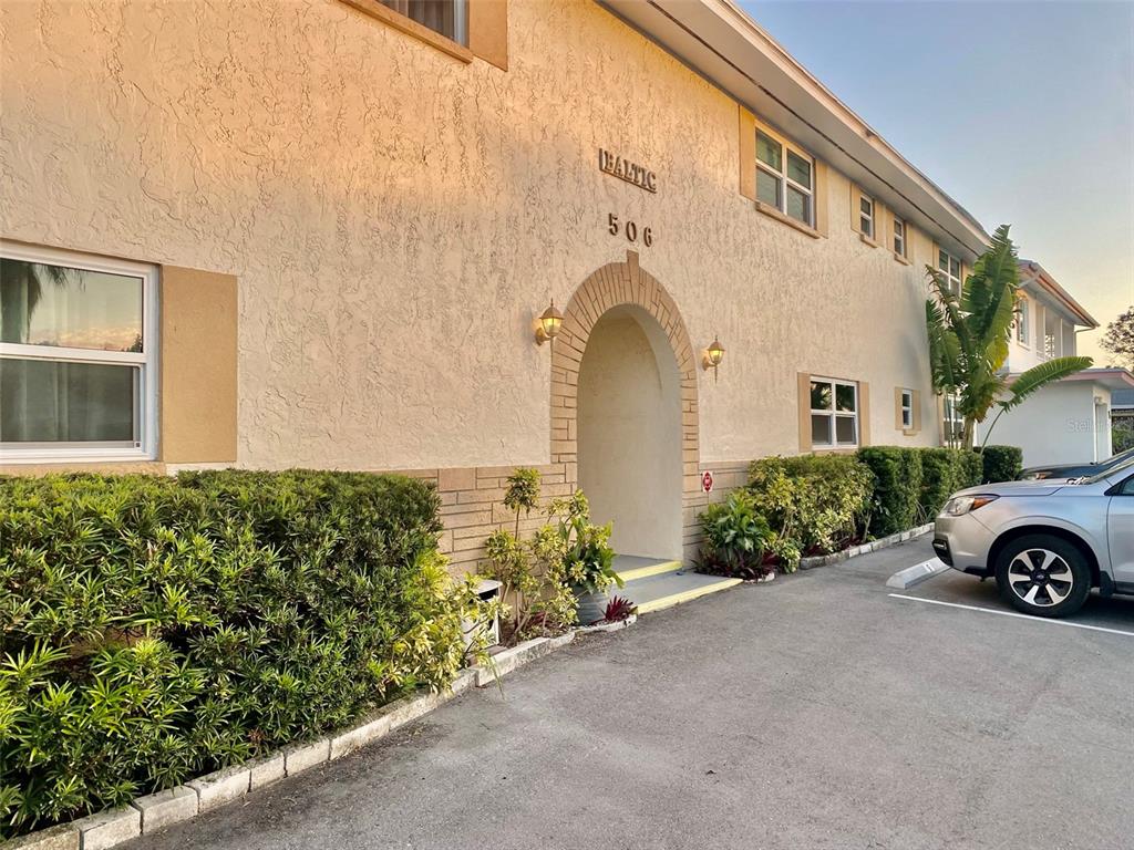 The exterior of a two-story apartment building features a stucco facade and an arched entryway — 506 71ST AVENUE UNIT 4, ST PETE BEACH, FL