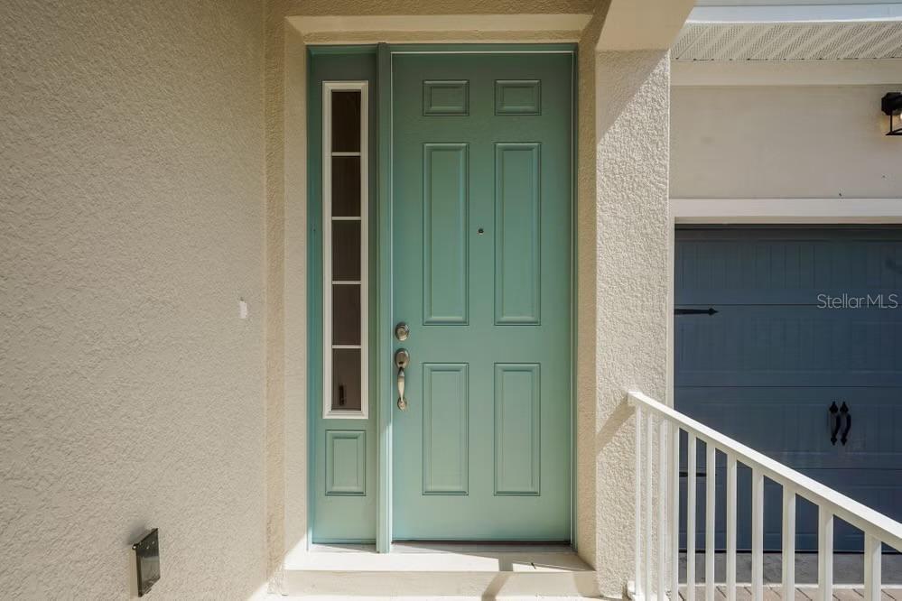 A teal front door with a side window light sits next to a garage door — 15075 TEA TREE DRIVE, WINTER GARDEN, FL