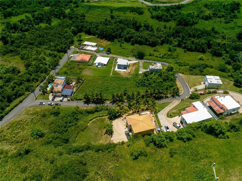 An aerial view shows several houses situated on a hillside surrounded by lush green vegetation — BO Mameyes LINDOMAR II Lote 24, RIO GRANDE, PR