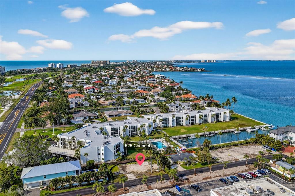 An aerial view shows a vacant waterfront lot situated next to a multi-story residential complex — 525 CHANNEL LANE, LONGBOAT KEY, FL