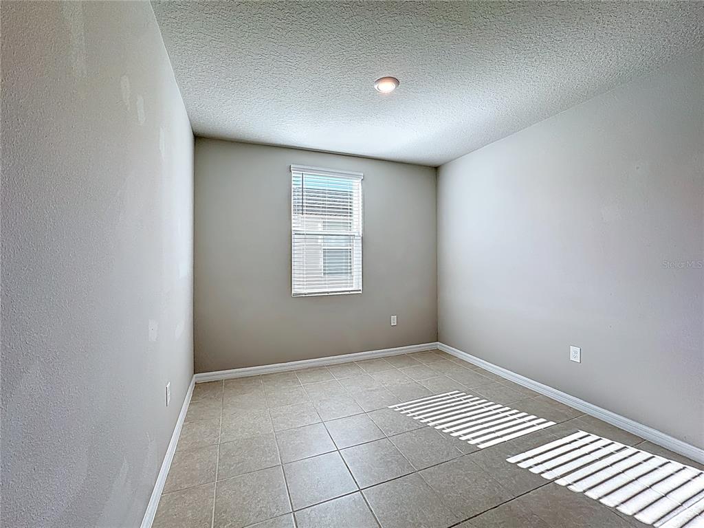 An empty room with beige walls, tile flooring, a single window, and a ceiling light — 5251 MEREDREW LANE, ST CLOUD, FL