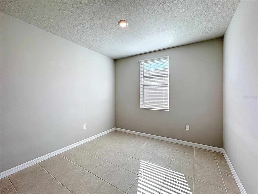 An empty room with light-colored walls, tile flooring, a single window, and a ceiling light — 5251 MEREDREW LANE, ST CLOUD, FL