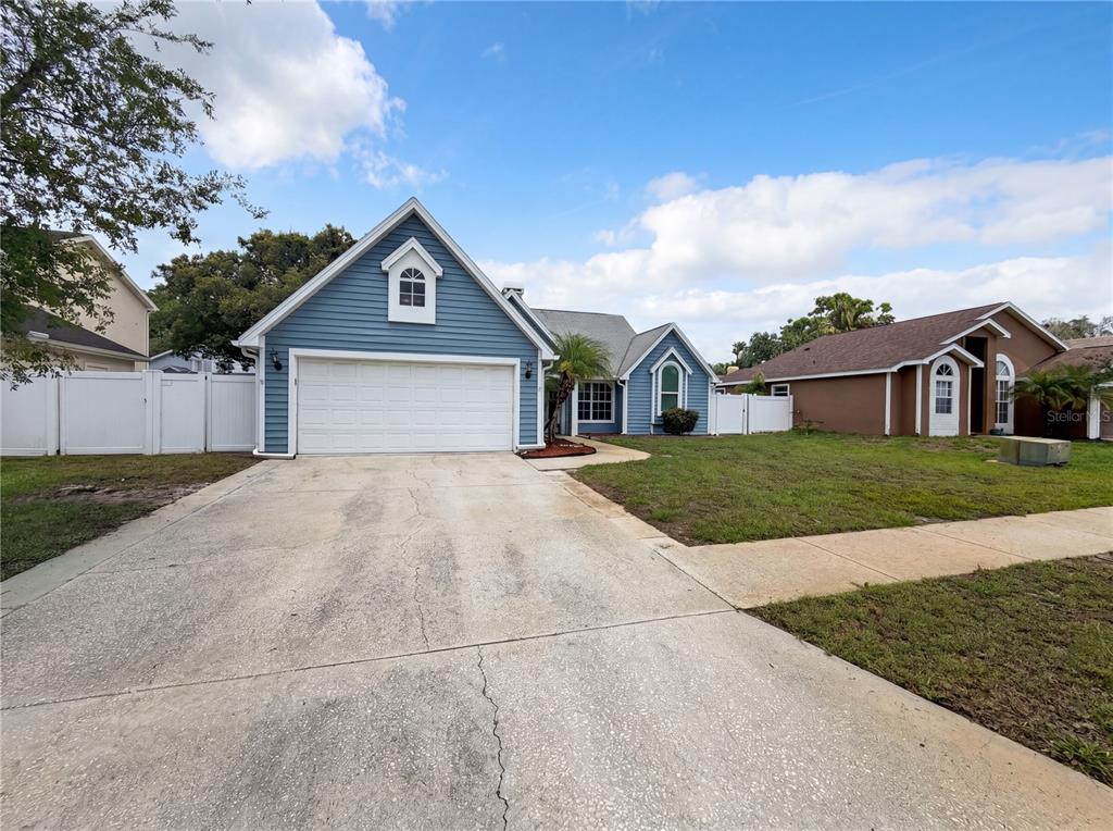A blue house with a white garage door and a concrete driveway under a sky — 7221 HIDEAWAY TRAIL, NEW PORT RICHEY, FL