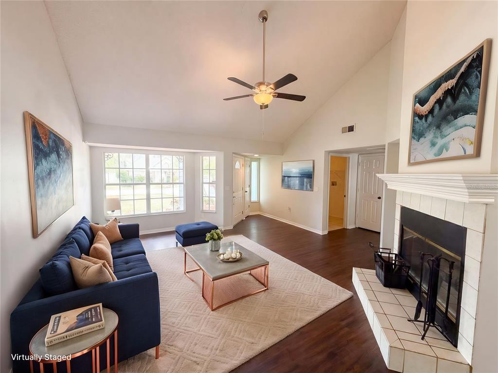 A living room with a fireplace, vaulted ceiling, ceiling fan, and dark wood flooring — 7221 HIDEAWAY TRAIL, NEW PORT RICHEY, FL