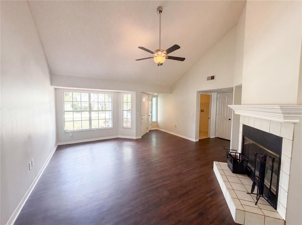 A living room with dark wood flooring, a vaulted ceiling, and a white brick fireplace — 7221 HIDEAWAY TRAIL, NEW PORT RICHEY, FL