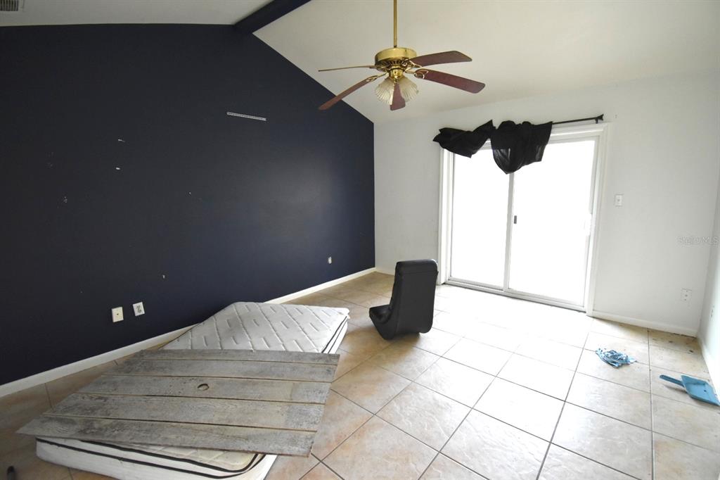An empty room features a dark accent wall, tile flooring, a ceiling fan, and sliding doors — 204 SHORE DRIVE W, OLDSMAR, FL