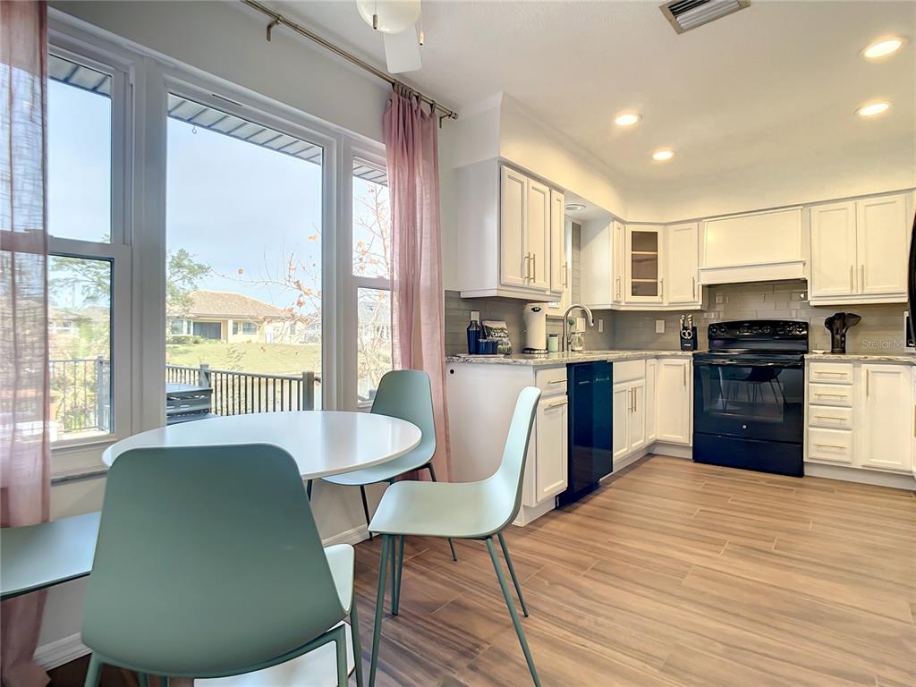A kitchen with white cabinets, black appliances, and a dining area overlooking a backyard — 12 COLLINSON COURT, PALM COAST, FL