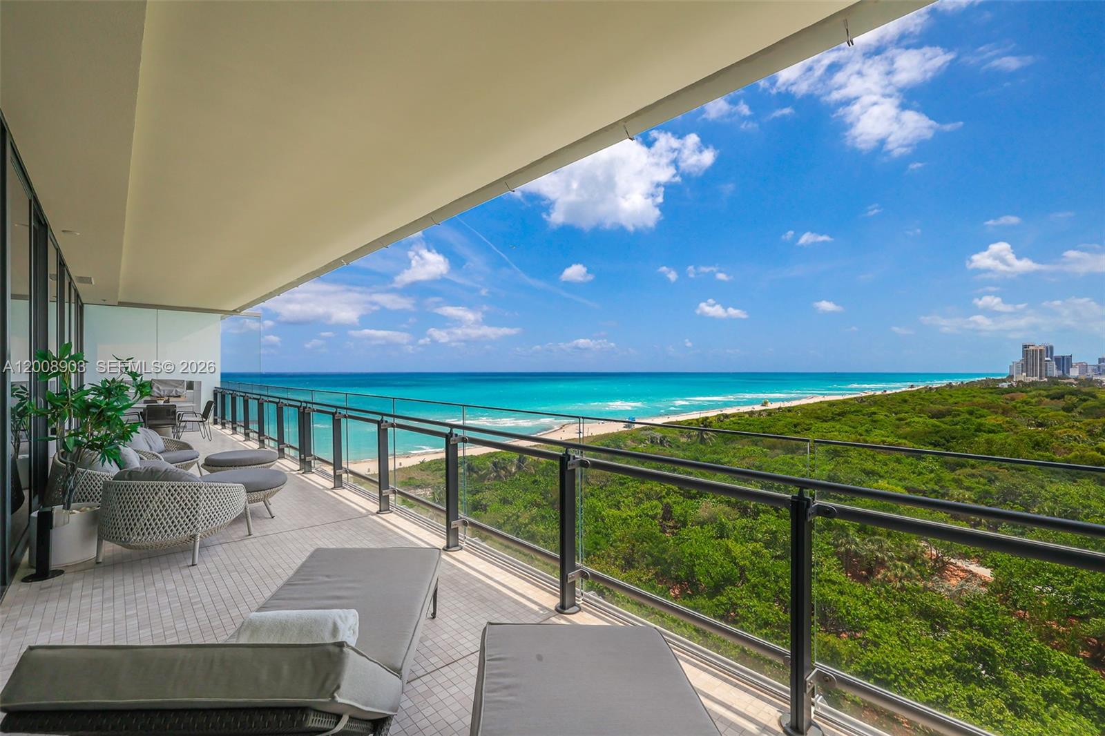 A spacious balcony features outdoor furniture overlooking a beach, ocean, and dense green forest — 8701 Collins Ave # 904, Miami Beach FL 33154, MIAMI BEACH, FL