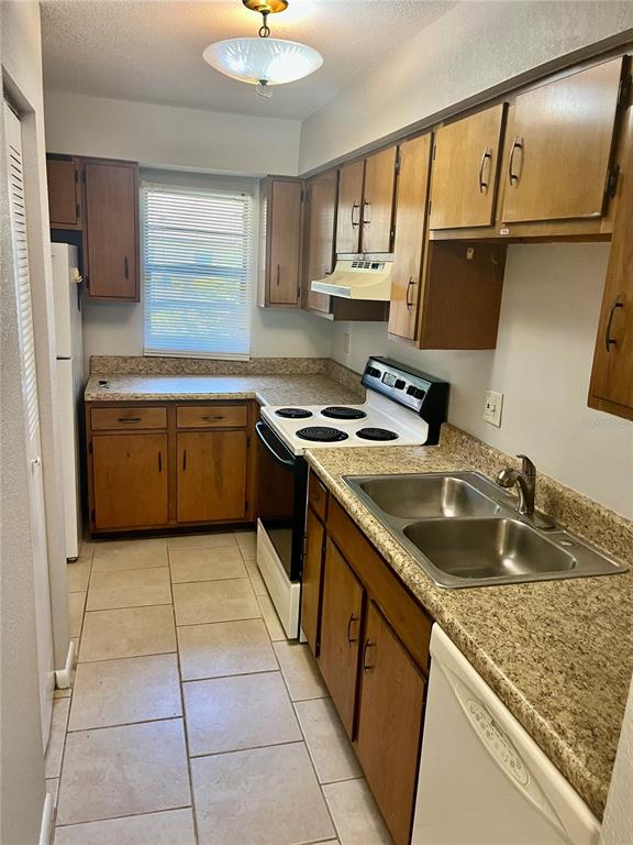 A kitchen features wood cabinets, laminate countertops, a white stove, and light-colored tile flooring — 3430 NW 21ST DRIVE UNIT D-2, GAINESVILLE, FL
