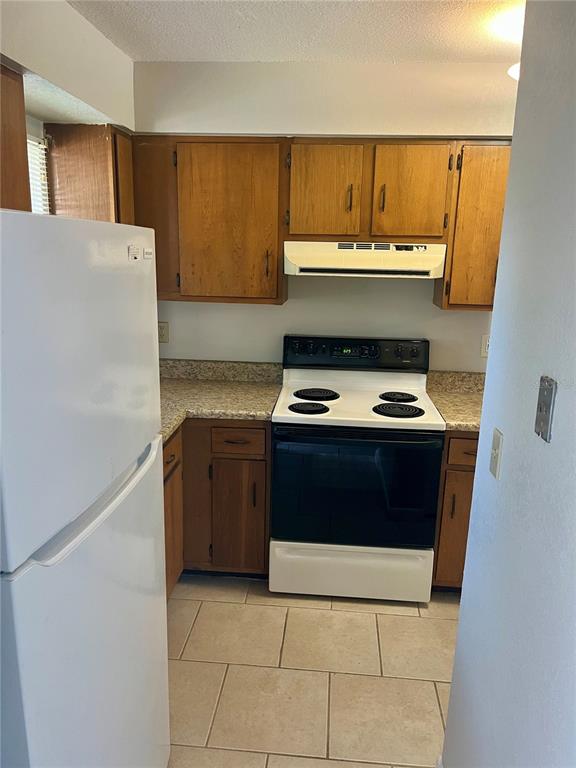 A kitchen with wood cabinets, a white stove, a white refrigerator, and tiled flooring — 3430 NW 21ST DRIVE UNIT D-2, GAINESVILLE, FL