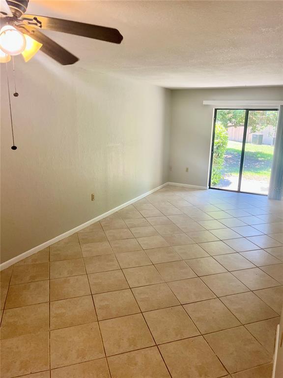 An empty room features beige tile flooring, a ceiling fan, and sliding glass patio doors — 3430 NW 21ST DRIVE UNIT D-2, GAINESVILLE, FL