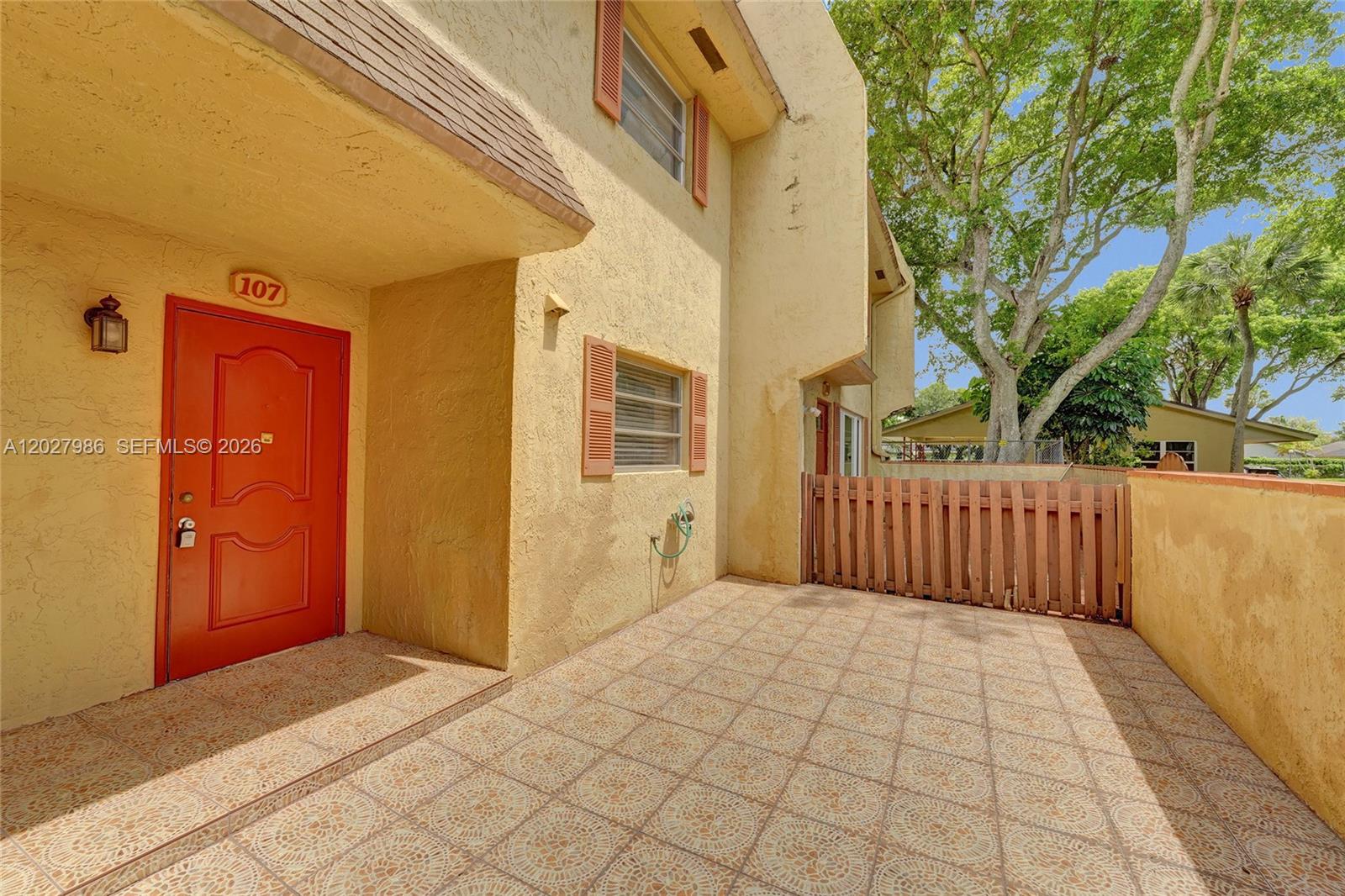 A yellow stucco building features a red front door and a tiled patio area — 7175 Nova Dr # 107, Davie FL 33317, DAVIE, FL