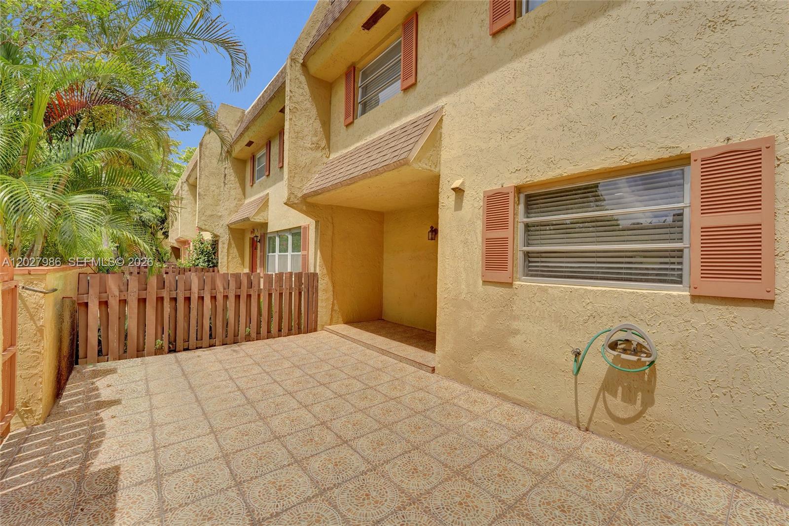 A paved patio sits in front of a two-story yellow townhouse with a wooden fence — 7175 Nova Dr # 107, Davie FL 33317, DAVIE, FL
