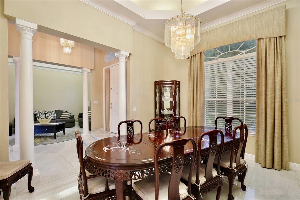 A formal dining room features a dark wood table, chandelier, and columns opening to a living area — 9374 WICKHAM WAY, ORLANDO, FL