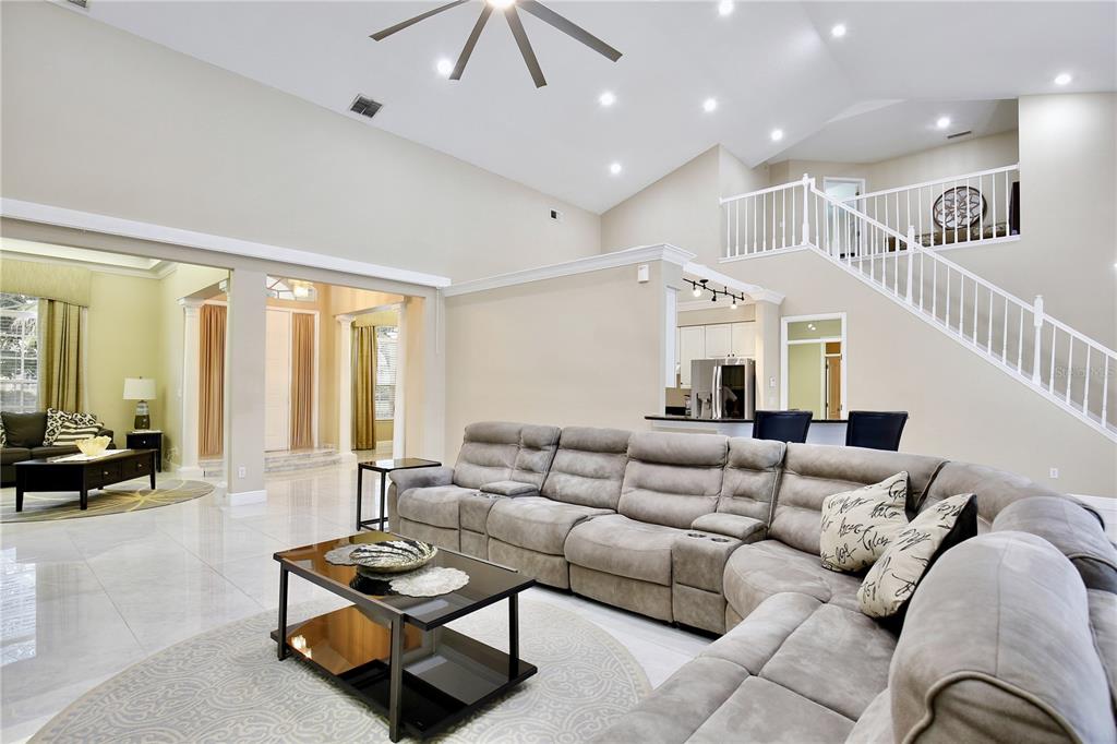 A spacious living room features a large sectional sofa, vaulted ceilings, and a staircase — 9374 WICKHAM WAY, ORLANDO, FL