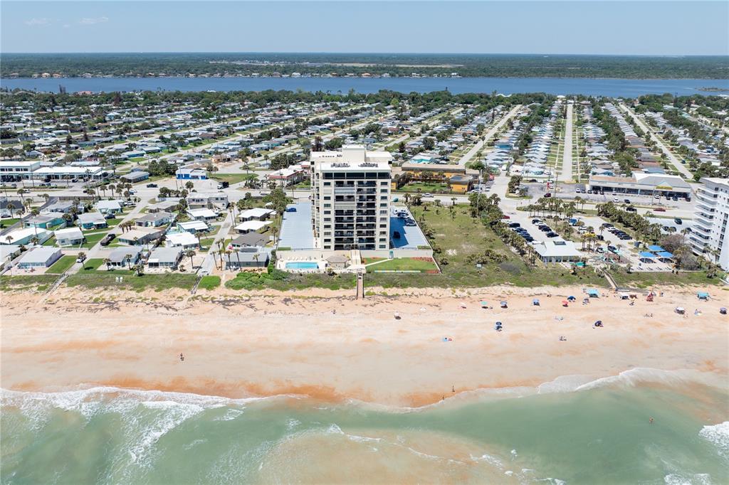 An aerial view shows a tall beachfront condominium building surrounded by houses and the ocean — 1513 OCEAN SHORE BOULEVARD UNIT 2C, ORMOND BEACH, FL
