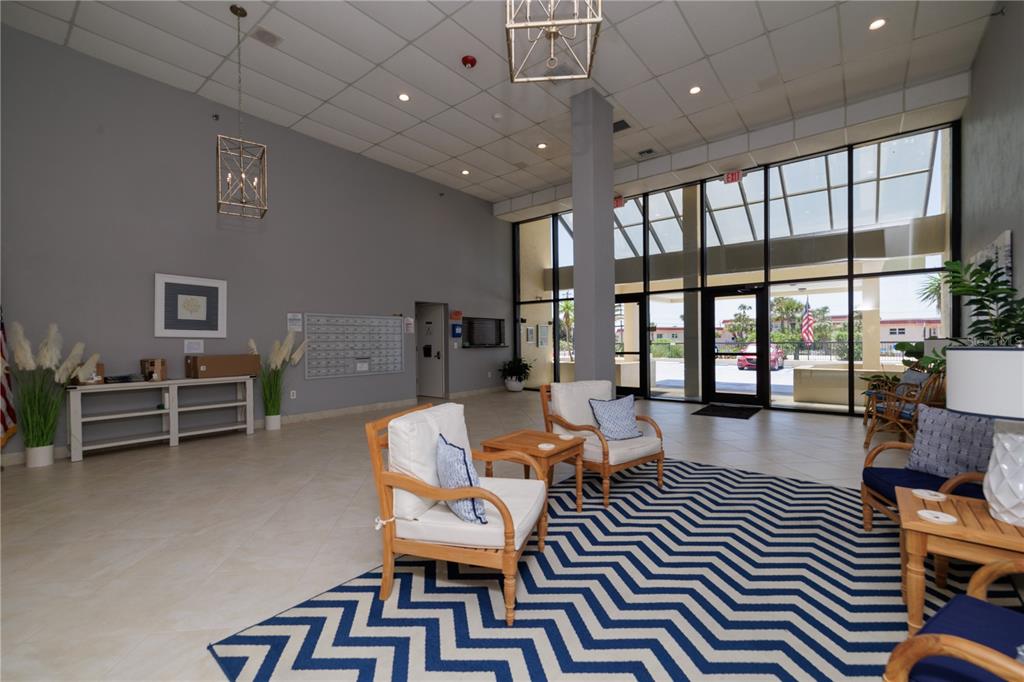 A bright lobby features a chevron rug, seating area, mailboxes, and floor-to-ceiling windows — 1513 OCEAN SHORE BOULEVARD UNIT 2C, ORMOND BEACH, FL